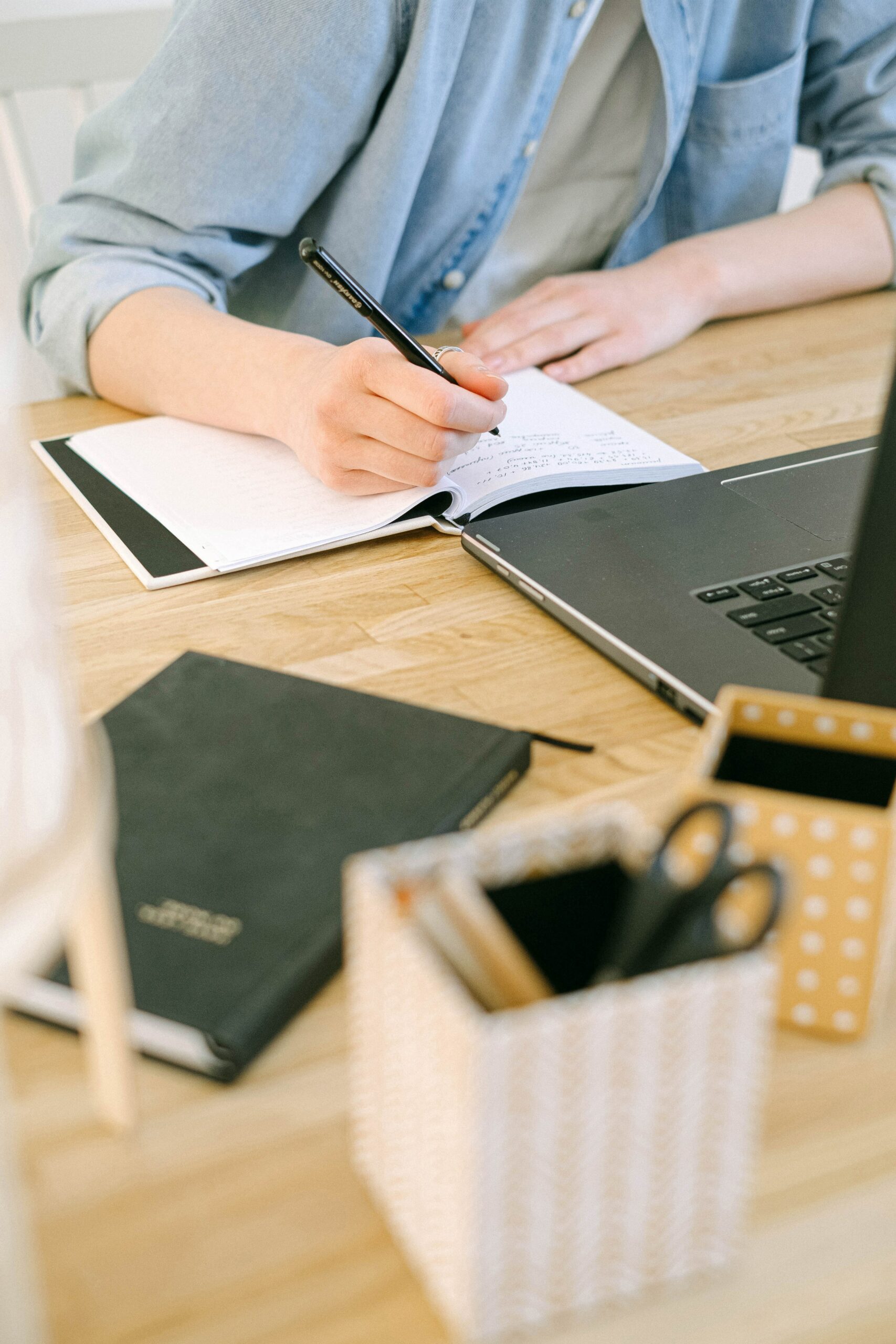 person writing in notebook in front of laptop
